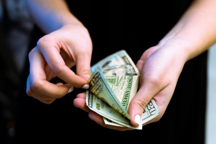 Orang yang memegang kipas uang kertas 100 dolar AS